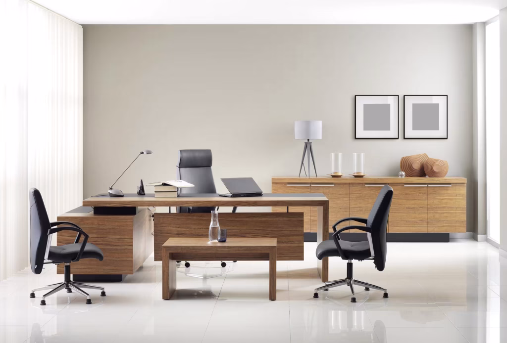 A modern office featuring a large wooden desk, black leather chairs, and a matching sideboard against a neutral wall with minimalist decor