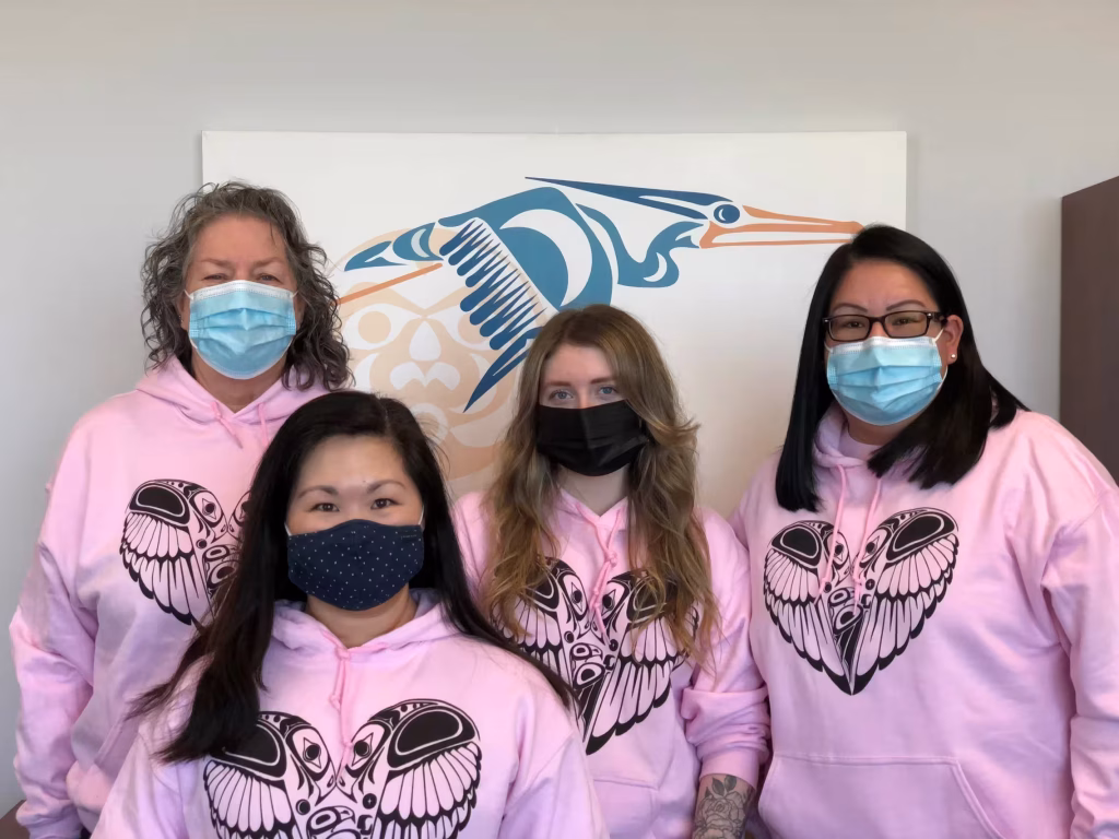 Four women wearing matching pink hoodies.