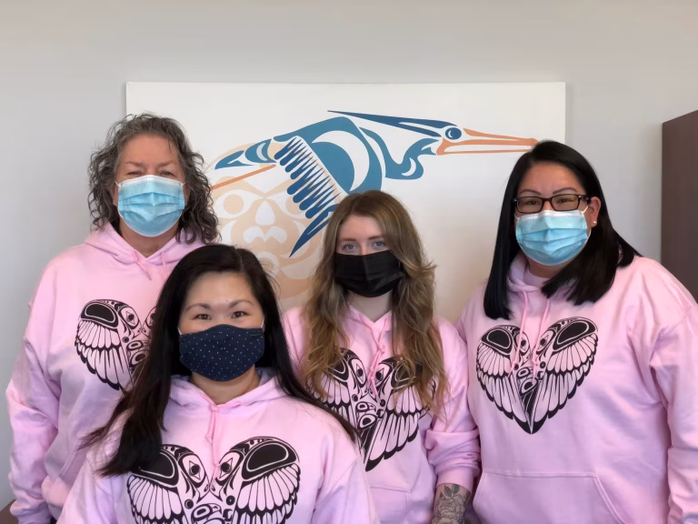 Four women wearing matching pink hoodies.
