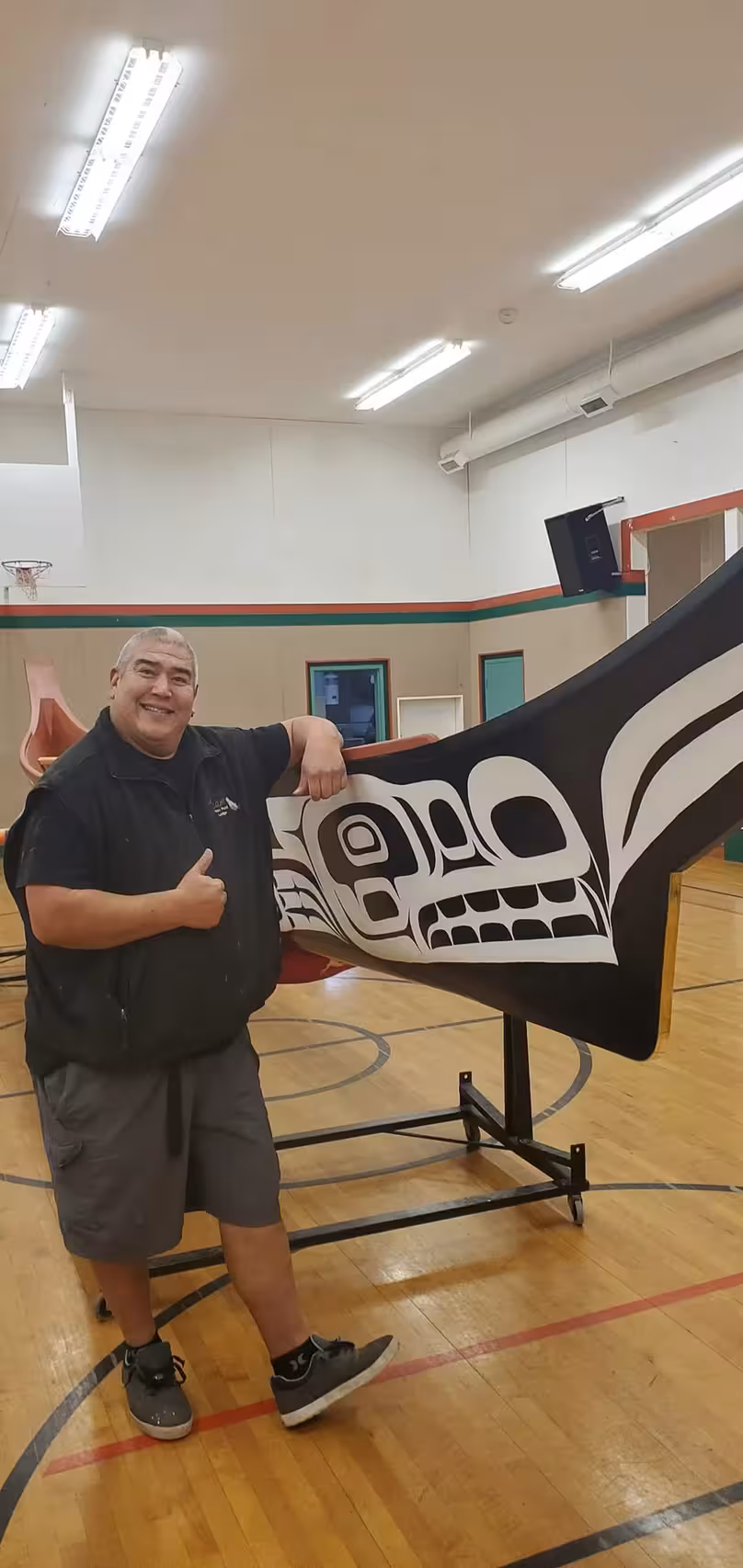 A man giving a thumbs up while leaning against a carved K’ómoks First Nation canoe.