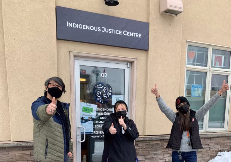 Three staff members giving thumbs up in front of an Indigenous Justice Centre