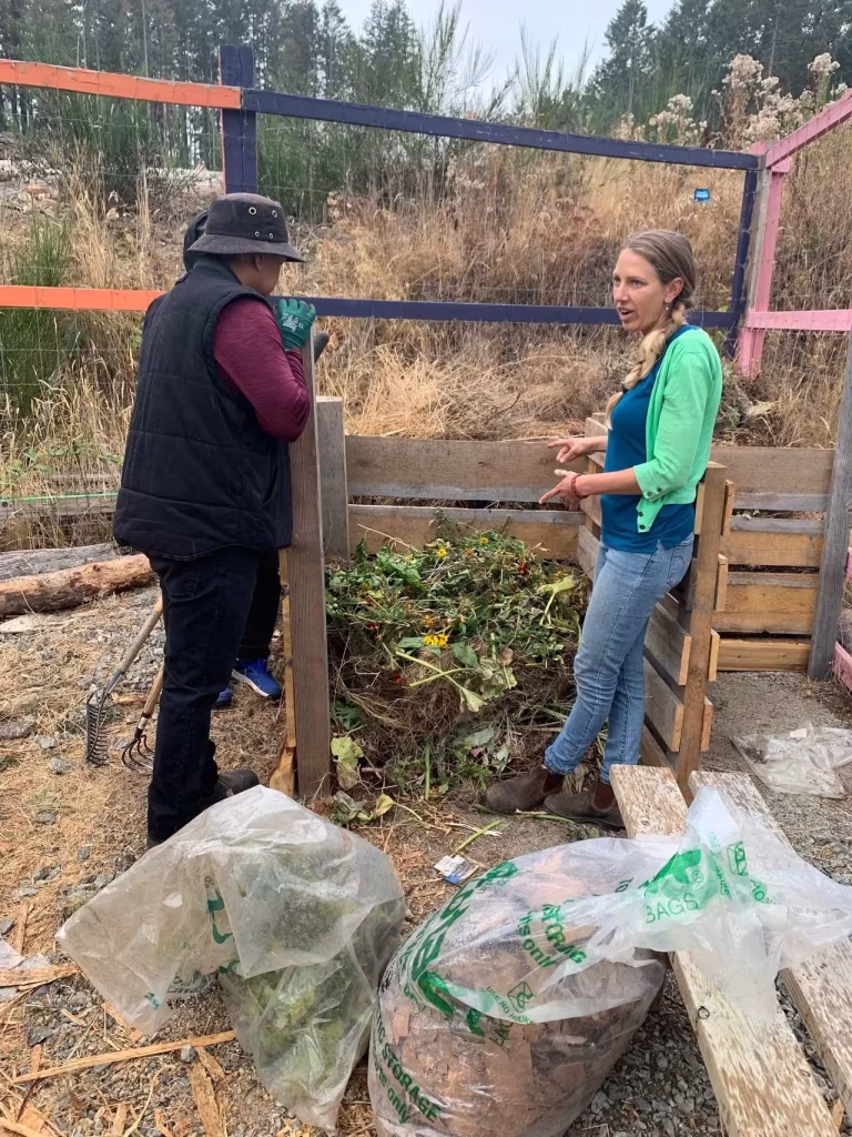 A woman talking about composting to another person at an outdoor wooden bin