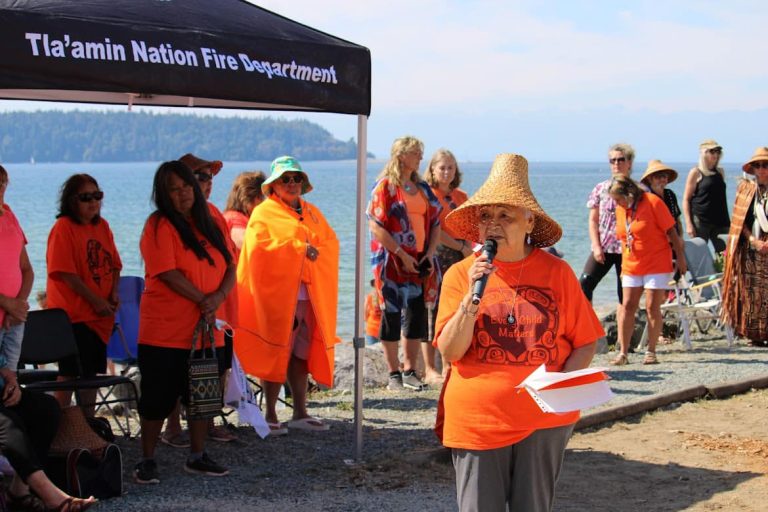 An Indigenous Elder speaking into a microphone at an event by the ocean