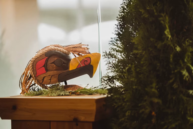A carved Indigenous bird mask on a wooden display