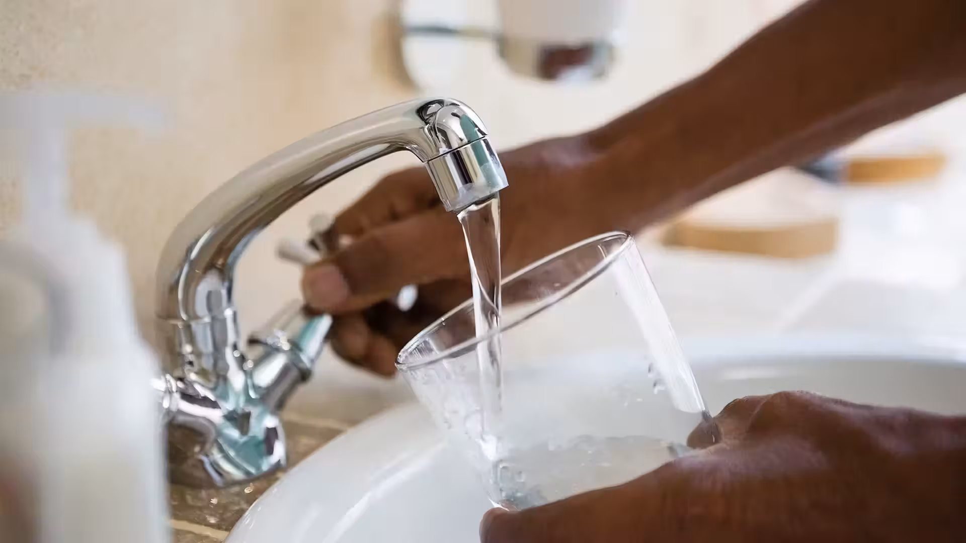 Close up of hands filling a clear glass with water from a chrome faucet