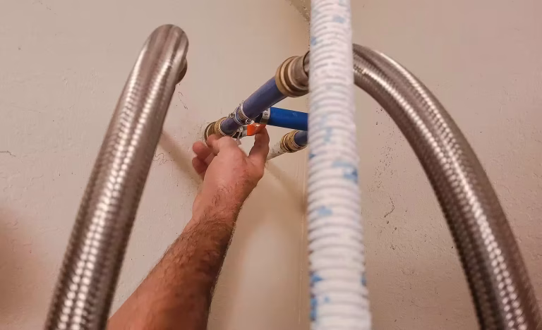 A person's hand adjusting a plumbing valve with blue PEX piping and braided hoses