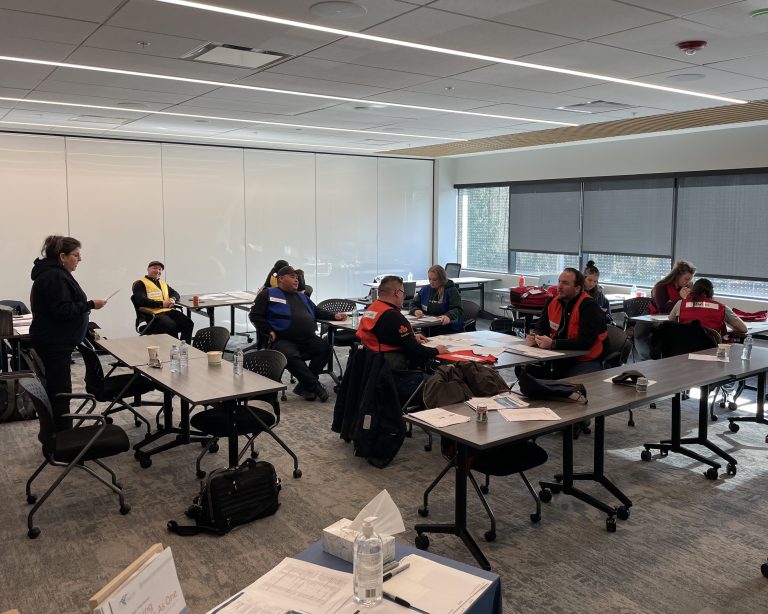 People in a training room wearing safety vests participate in a tabletop emergency preparedness exercise.