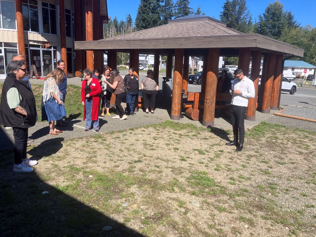 A group of people stand outside a building with a covered outdoor seating area.
