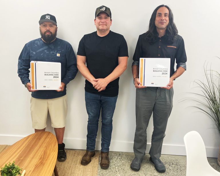 Three men stand holding binders labeled "British Columbia Building Code 2024.