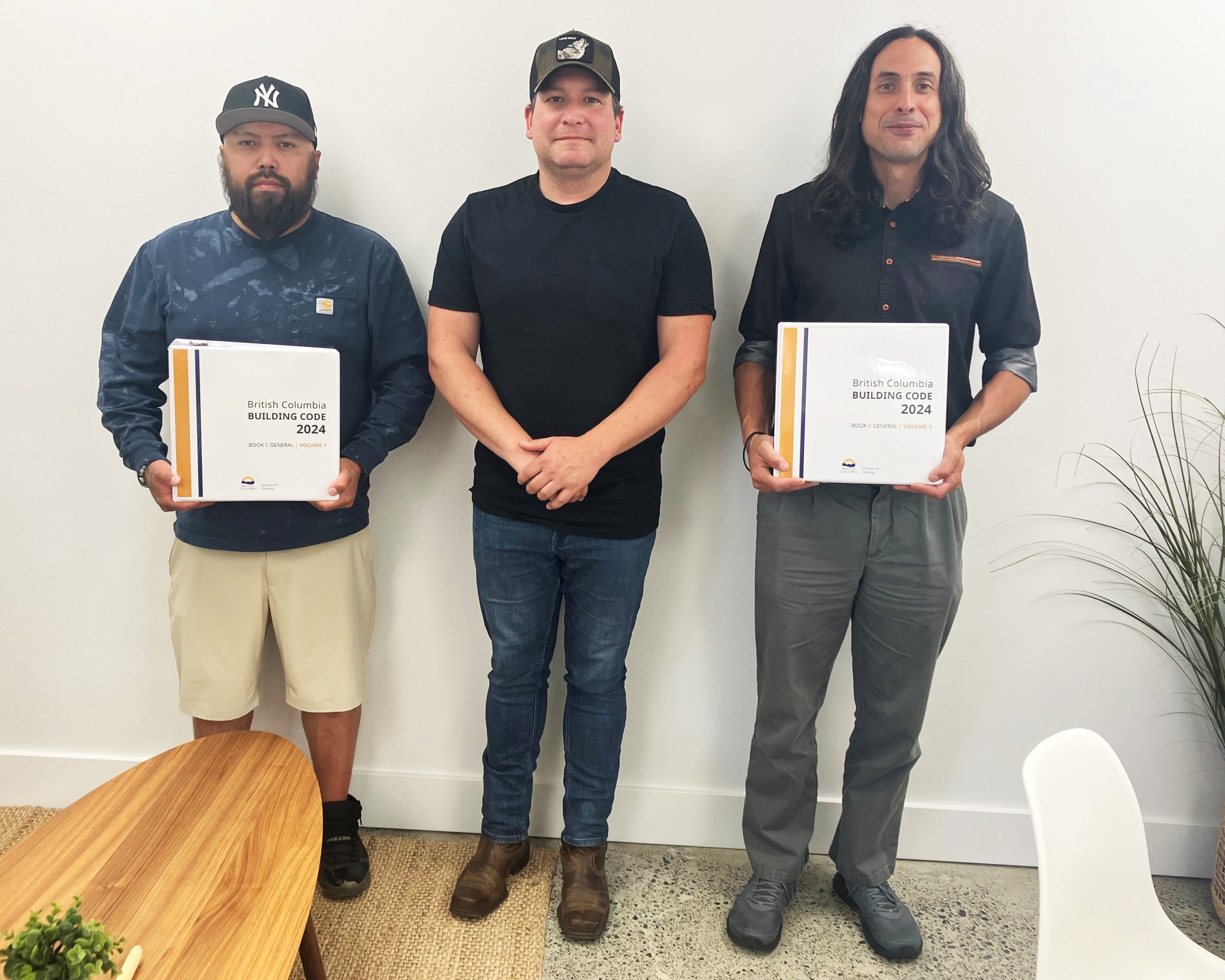 Three men stand holding binders labeled "British Columbia Building Code 2024.
