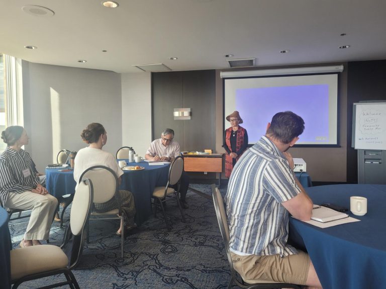 People attend a planning meeting with a presenter by a projector screen and whiteboard.